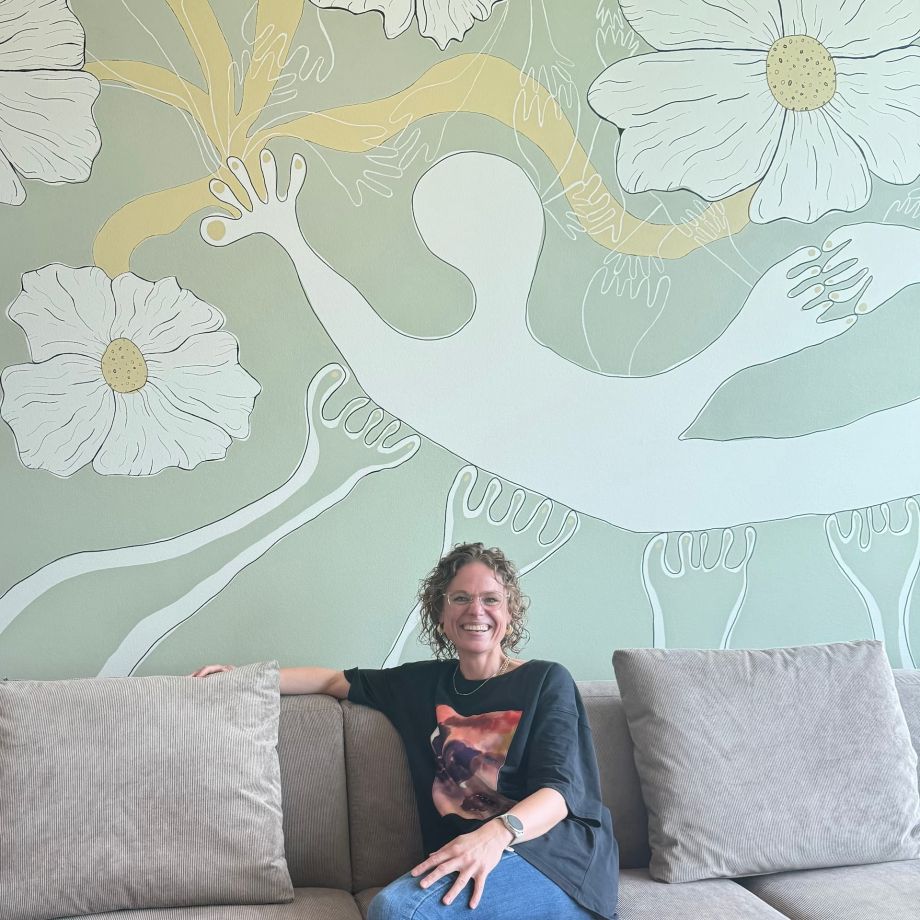 Kunstværk på papir lavet med farvet kul hænger ved et vindue i en minimalistisk indrettet krog af rummet. Ved siden af står en vase med blomster og en lille guldfarvet lampe. Det abstrakte værk afspejler en figur, der forsøger at finde vej gennem livets følelsesmæssige uro.