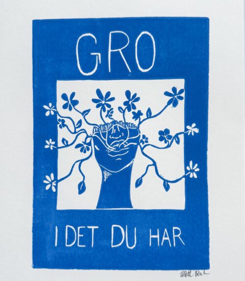 Nærbillede af linoleumstrykket “Gro i det du har” i blå og hvid. En hånd i midten griber omkring blomstrende grene, og omgivelserne er fyldt med blomster. Teksten “GRO I DET DU HAR” er håndskrevet i værket. Kunsttrykket udstråler håb, styrke og bevidsthed.
